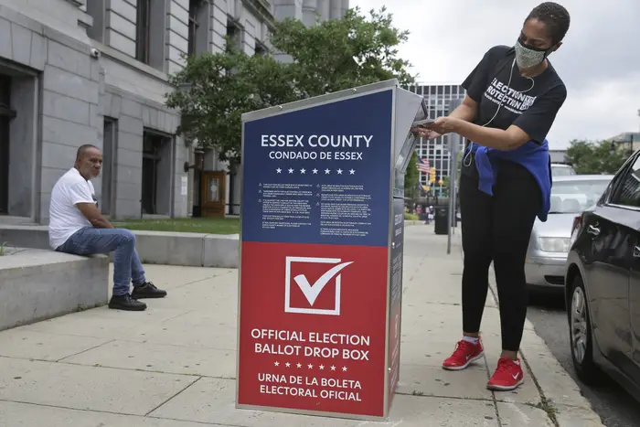 A NJ resident drops her mail-in ballot into a drop box in Newark